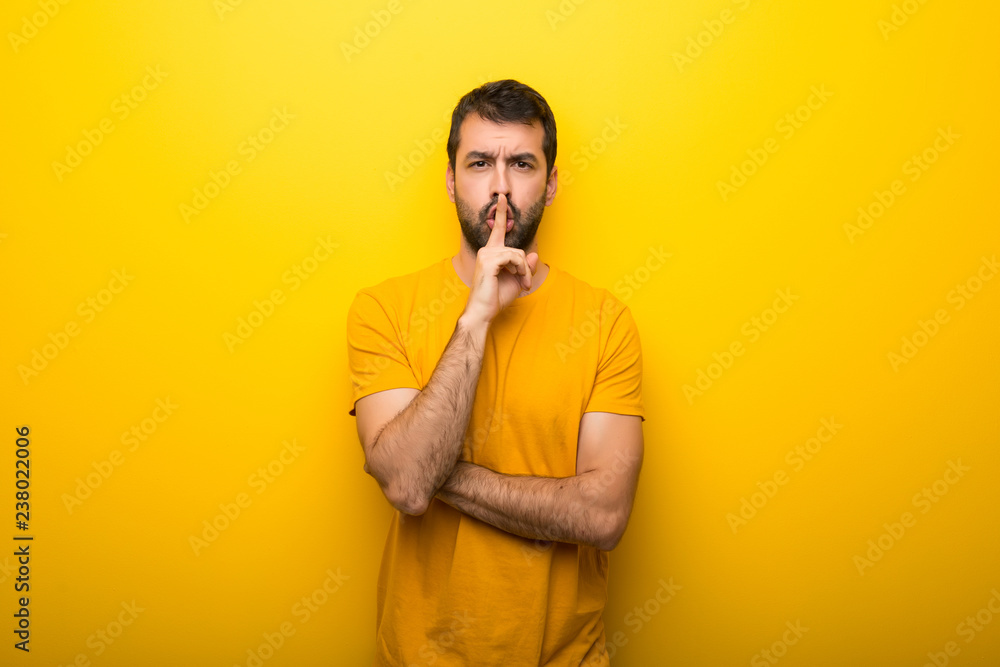 Man on isolated vibrant yellow color showing a sign of silence gesture putting finger in mouth Man on isolated vibrant yellow color showing a sign of silence gesture putting finger in mouth