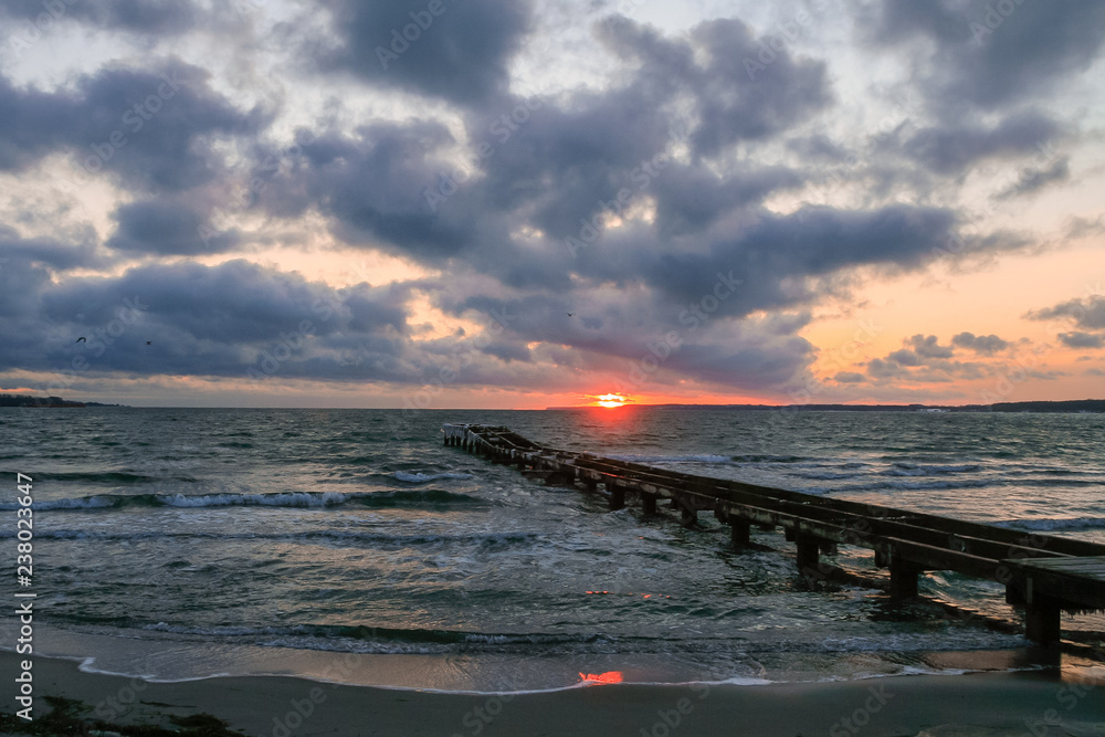 seascape with romantic pier, clouds and waves at sunrise