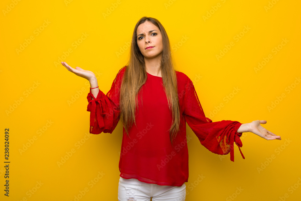 Young girl with red dress over yellow wall unhappy and frustrated with something because not understand something Young girl with red dress over yellow wall unhappy and frustrated with something because not understand something