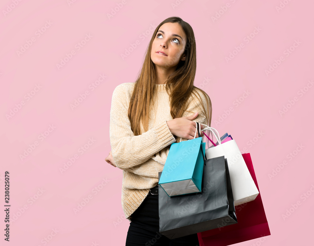 Young girl with shopping bags with confuse face expression while bites lip on isolated pink background
