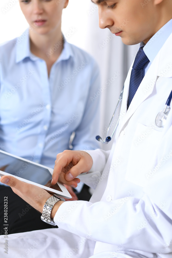 Male doctor using touchpad or tablet pc while consulting female patient in hospita. Medicine and healthcare concept Male doctor using touchpad or tablet pc while consulting female patient in hospita. Medicine and healthcare concept