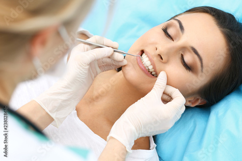 Young female patient visiting dentist office.Beautiful woman with healthy straight white teeth sitting at dental chair with open mouth during oral checkup while doctor working at teeth