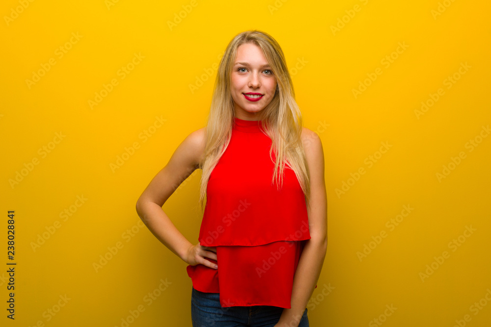 Young girl with red dress over yellow wall posing with arms at hip and smiling Young girl with red dress over yellow wall posing with arms at hip and smiling