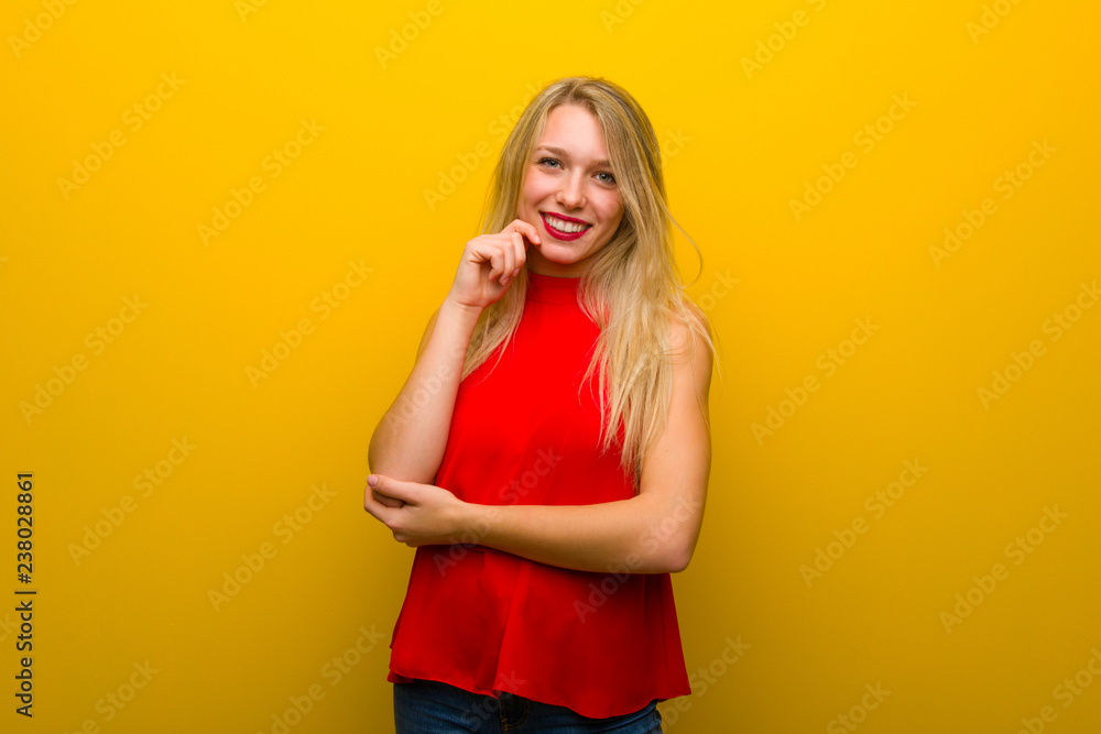Young girl with red dress over yellow wall smiling with a sweet expression Young girl with red dress over yellow wall smiling with a sweet expression