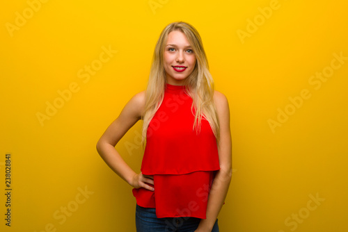 Young girl with red dress over yellow wall posing with arms at hip and smiling