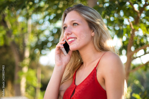 Young blonde girl keeping a conversation with the mobile phone with someone at outdoor