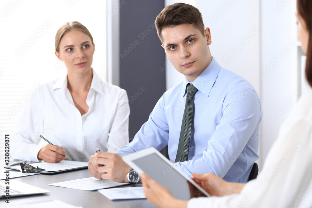 Group of business people or lawyers discussing terms of transaction in office. Colleagues working all together. Focus on young businessman. Meeting and teamwork concept Group of business people or lawyers discussing terms of transaction in office. Colleagues working all together. Focus on young businessman. Meeting and teamwork concept