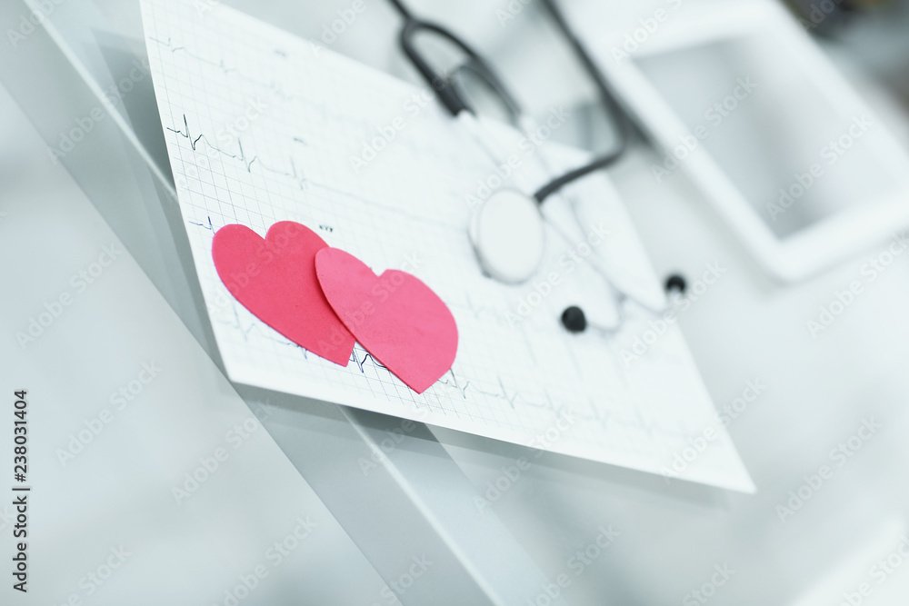 Fototapeta premium stetoskop, kardiogram i dwa czerwone papierowe serca na stole.