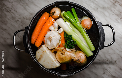 Clear Chicken broth with pieces of  vegetables in a metal pot before cooking with crystal water.  Chicken Soap with a lot of vegetables in preparation process  in a saucepan. photo