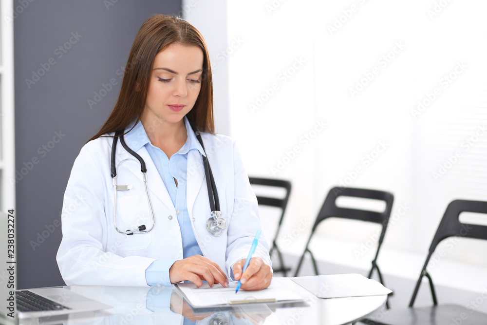 Doctor woman at work. Portrait of female physician filling up medical form while sitting at the glass desk at clinic or hospital. Medicine and healthcare concept Doctor woman at work. Portrait of female physician filling up medical form while sitting at the glass desk at clinic or hospital. Medicine and healthcare concept