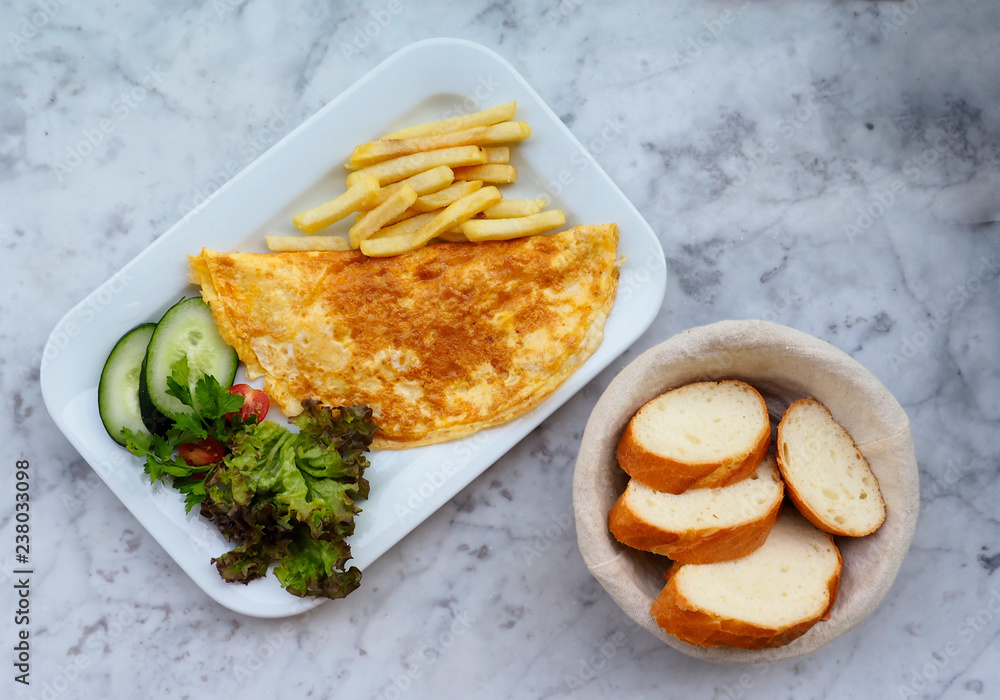  Omelette in a plate on marble background, top view. Omelette with cherry tomatoes, salad, cucumber and french fries. Flat lay breakfast with omelette, vegetables and bread basket. 