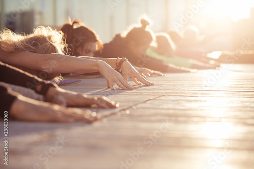 Fototapeta Naklejka Na Ścianę i Meble -  Child exercise, Balasana pose, working out. Yoga class. Group of sporty people doing yoga exercises in the morning at sunrise. Cropp shoot, sunny rays, healfy and calm concept, copy space