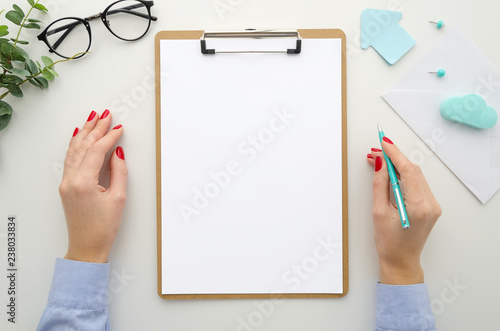 Business woman in blue shirt holds pen. lipboard mockup A4 size isolated on white desk, office supplies, eyeglasses, envelope. Top view flat lay. Template for reports, resume, brief, form, contract photo