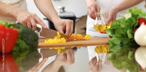 Closeup of human hands cooking in kitchen. Mother and daughter or two female friends cutting vegetables for fresh salad. Friendship, family dinner and lifestyle concepts