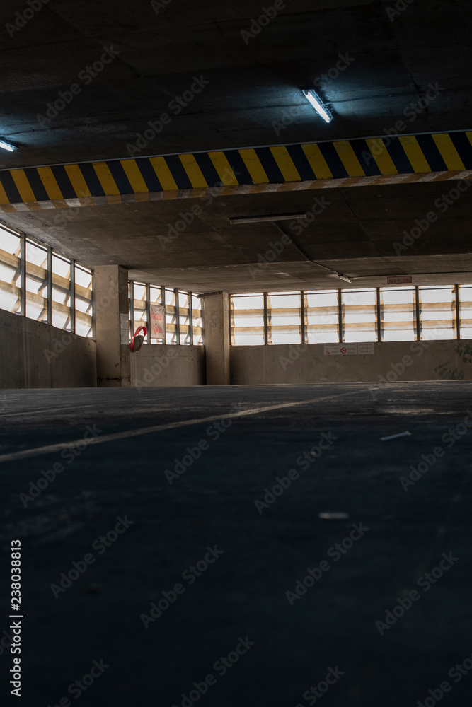A view of an old parking lot on 3th floor of a parking building in a business district with a low key. Seeing yellow and black traffic sign warning the height of the ceiling.