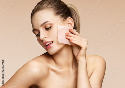 Woman cleaning face with facial cleansing wipes, removing makeup. Photo of woman with perfect skin on beige background. Beauty concept