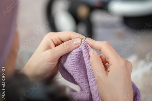 Close-up female hands knitting outdoors. Woman knitting in park during walk with baby in stroller. Process of needlework