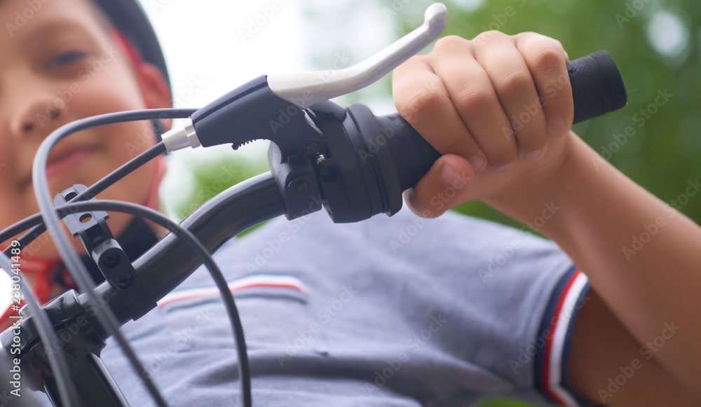 Teenager boy in protective helmet sitting on his bicycle in park on summer day. Selective focus.