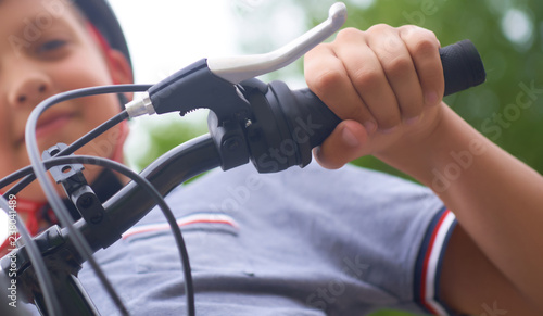 Teenager boy in protective helmet sitting on his bicycle in park on summer day. Selective focus.