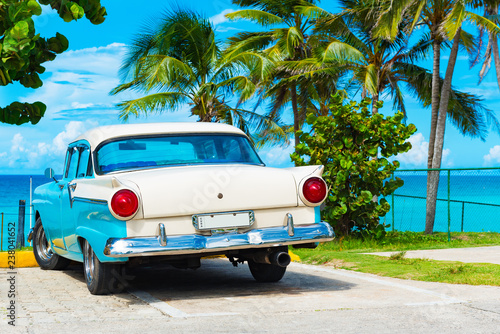 Fototapeta Naklejka Na Ścianę i Meble -  Amerikanischer Oldtimer parkt am Strand von Havanna unter Palmen in Kuba - Serie Kuba Reportage