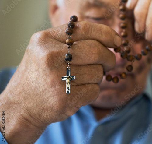 Praying old man with hands holding rosary beads.