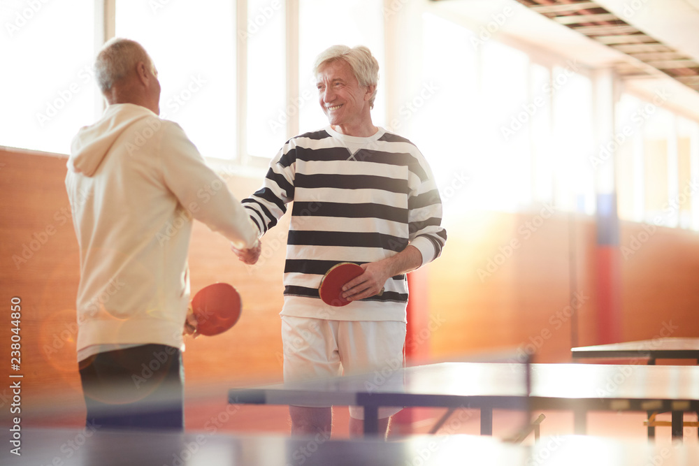 Two senior ping pong players shaking hands after or before game while standing by table Stock