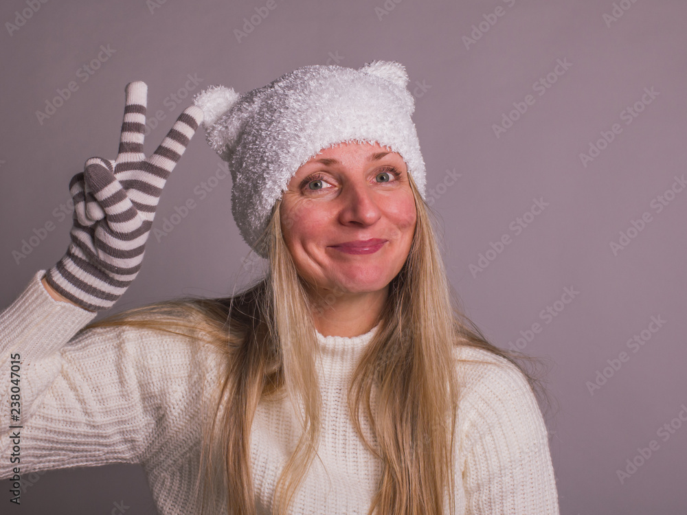Obraz premium happy adult woman in funny kids hat with ears showing the sign of victory, hand in striped gloves
