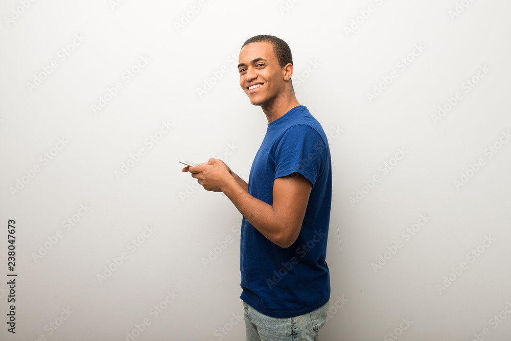 Young african american man on white wall sending a message with the mobile Young african american man on white wall sending a message with the mobile