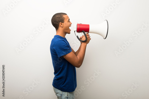 Young african american man on white wall shouting through a megaphone to announce something in lateral position