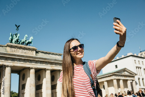 Photography Young beautiful positive girl makes selfie against the background of the Brandenburg Gate in Berlin in Germany or takes pictures of sights
