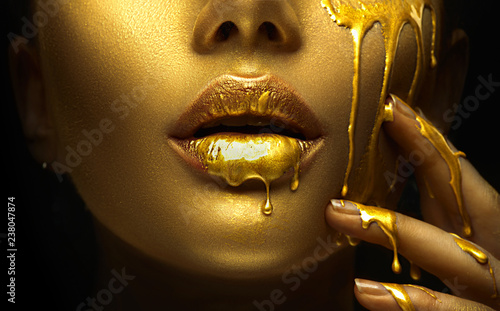 Golden paint smudges drips from the face lips and hand, golden liquid drops on beautiful model girl's mouth, creative abstract makeup. Beauty woman face © Subbotina Anna