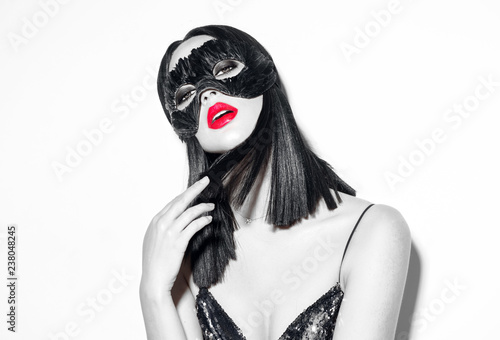 Beauty sexy brunette woman portrait. Girl wearing carnival black feather mask. Black hair, red lips, holiday makeup. Black and white fashion portrait