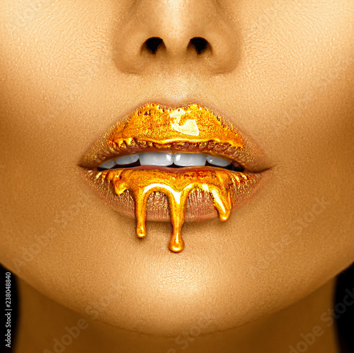 Gold paint drips from the sexy lips, golden liquid drops on beautiful model girl's mouth, creative abstract makeup. Beauty woman face © Subbotina Anna