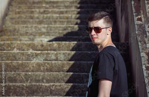 Portrait of handsome brunet young man wearing casual clothing and sunglasses, with old stairs on background.