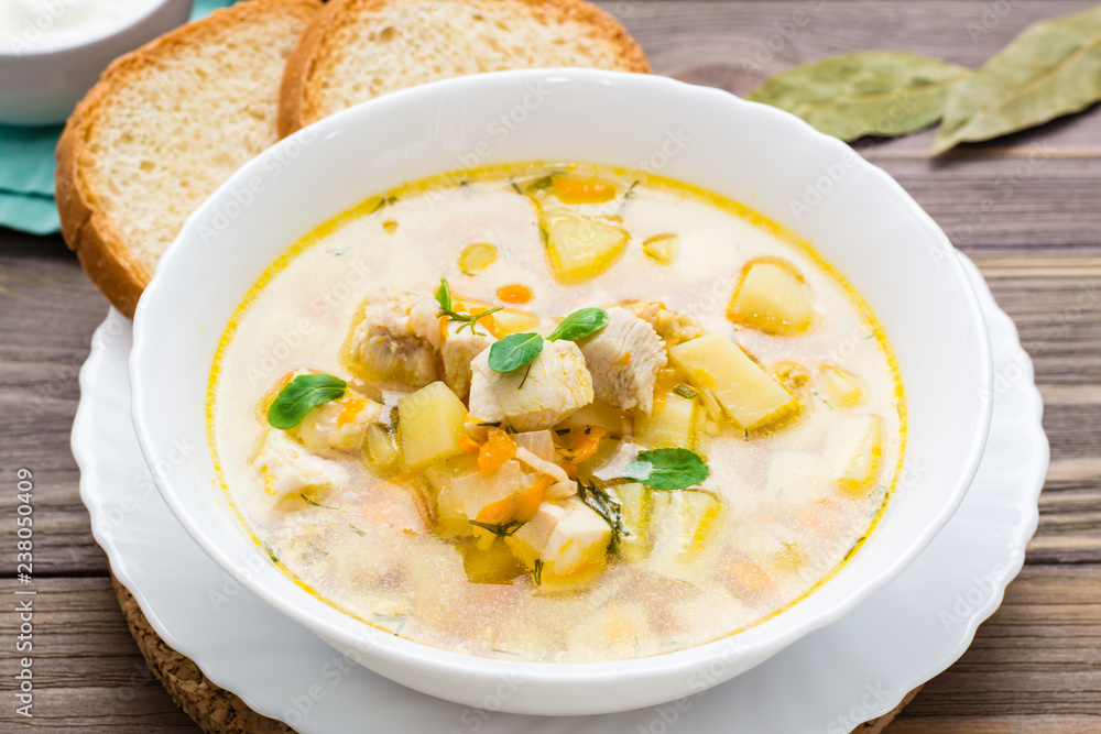Fresh chicken broth soup with potatoes and herbs in a white bowl on a wooden table Fresh chicken broth soup with potatoes and herbs in a white bowl on a wooden table
