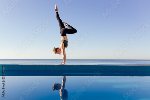 Fototapeta Young attractive woman practicing yoga doing Variation of handstand pose, Pincha Mayurasana