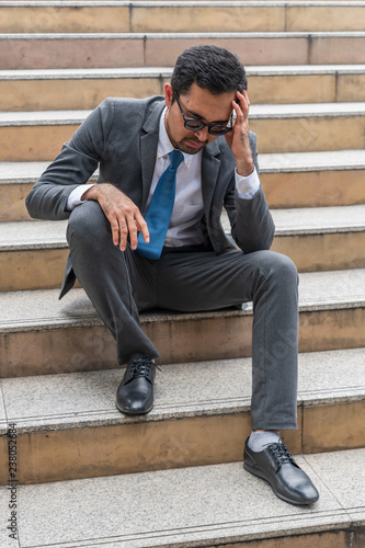 A sad looking young businessman sitting at the staircase looking down with stressed and depressed look gesture © phichak
