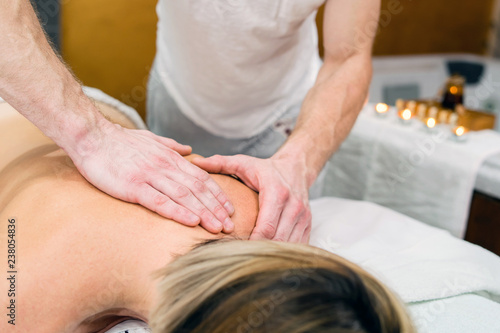 woman getting massage on her shoulder by therapist in spa salon
