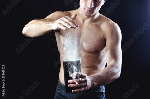 Canvas-taulu Young strong athlete pours protein nutrition supplement into a black plastic shaker on a dark studio background