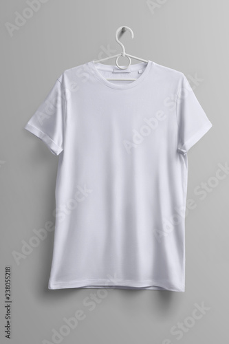 White T-shirt hanging on a plastic hanger with shadows on a studio gray background.