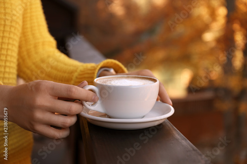 Woman in warm sweater holding cup with hot cozy drink on wooden railing at balcony