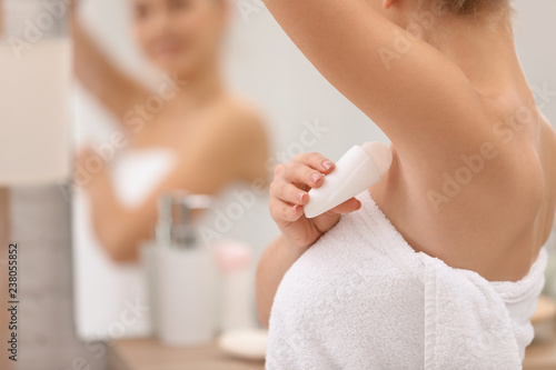 Beautiful young woman applying deodorant after shower in bathroom. Space for text
