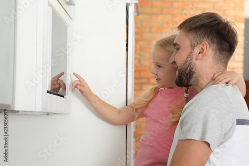 Little daughter and father using microwave oven in kitchen