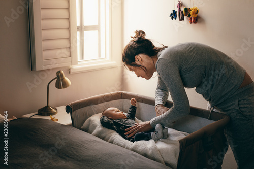 Cuadro en lienzo Young mother looking at her baby sleeping in a crib