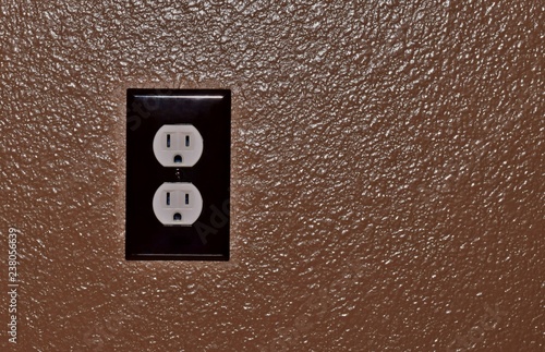 An off-center image of a power outlet fixed to a brown textured wall.