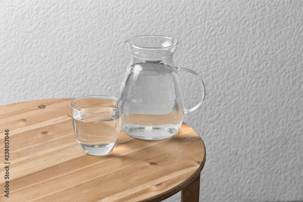 Obraz premium Pitcher and glass with water on table near white wall. Space for text