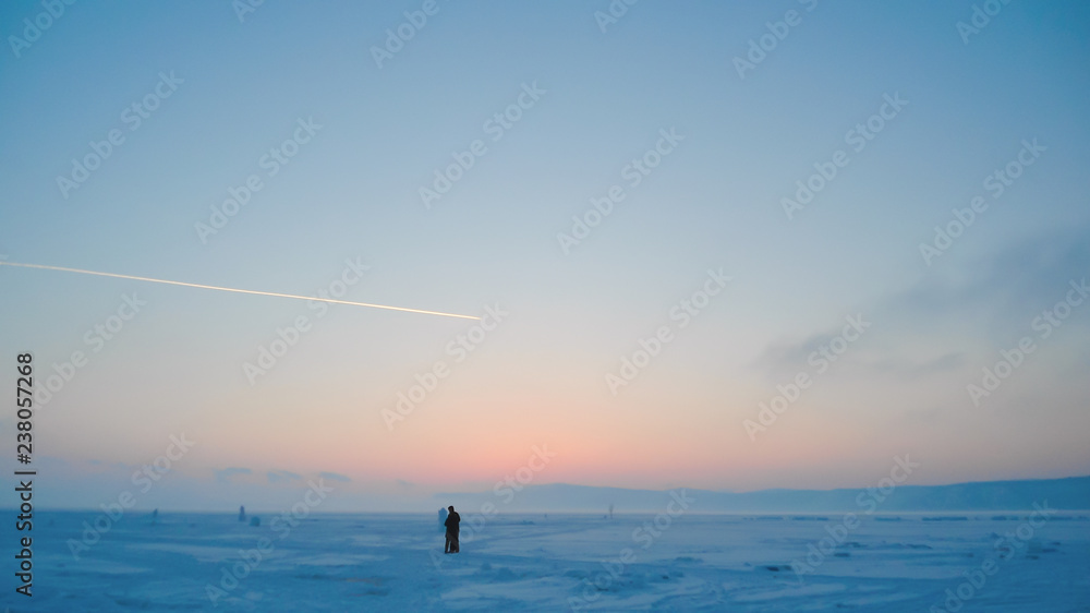 Fototapeta premium a couple in love on a romantic walk through a snowy field at sunset; winter cold; blue frosty haze over a frozen lake