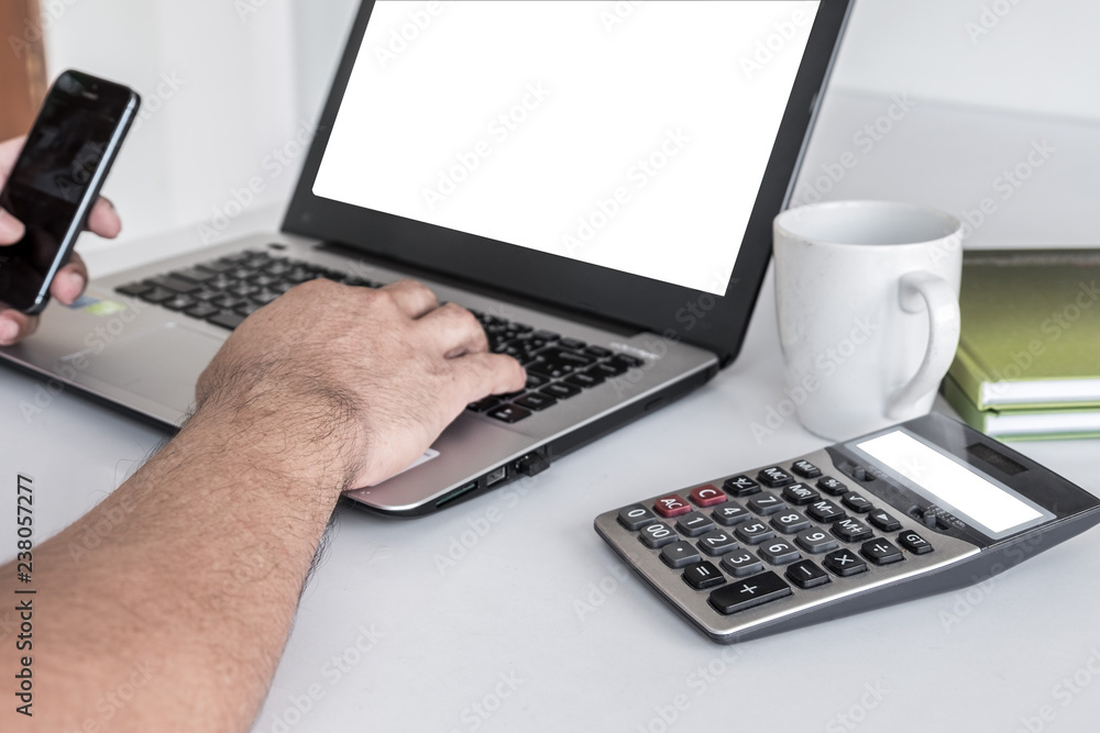 Men's hands are pressing the cell phone. And have a laptop white screen. calculator white screen a pencil is placed on a notebook. on the white desk. Men's hands are pressing the cell phone. And have a laptop white screen. calculator white screen a pencil is placed on a notebook. on the white desk.