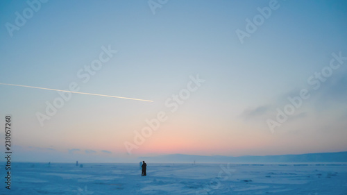 arctic landscape at sunset; silhouettes of young couple standing in the middle of snowy wide plain of a frozen lake