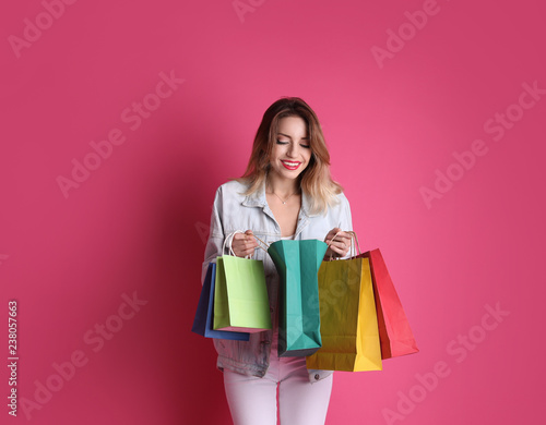 Beautiful young woman with shopping bags on color background